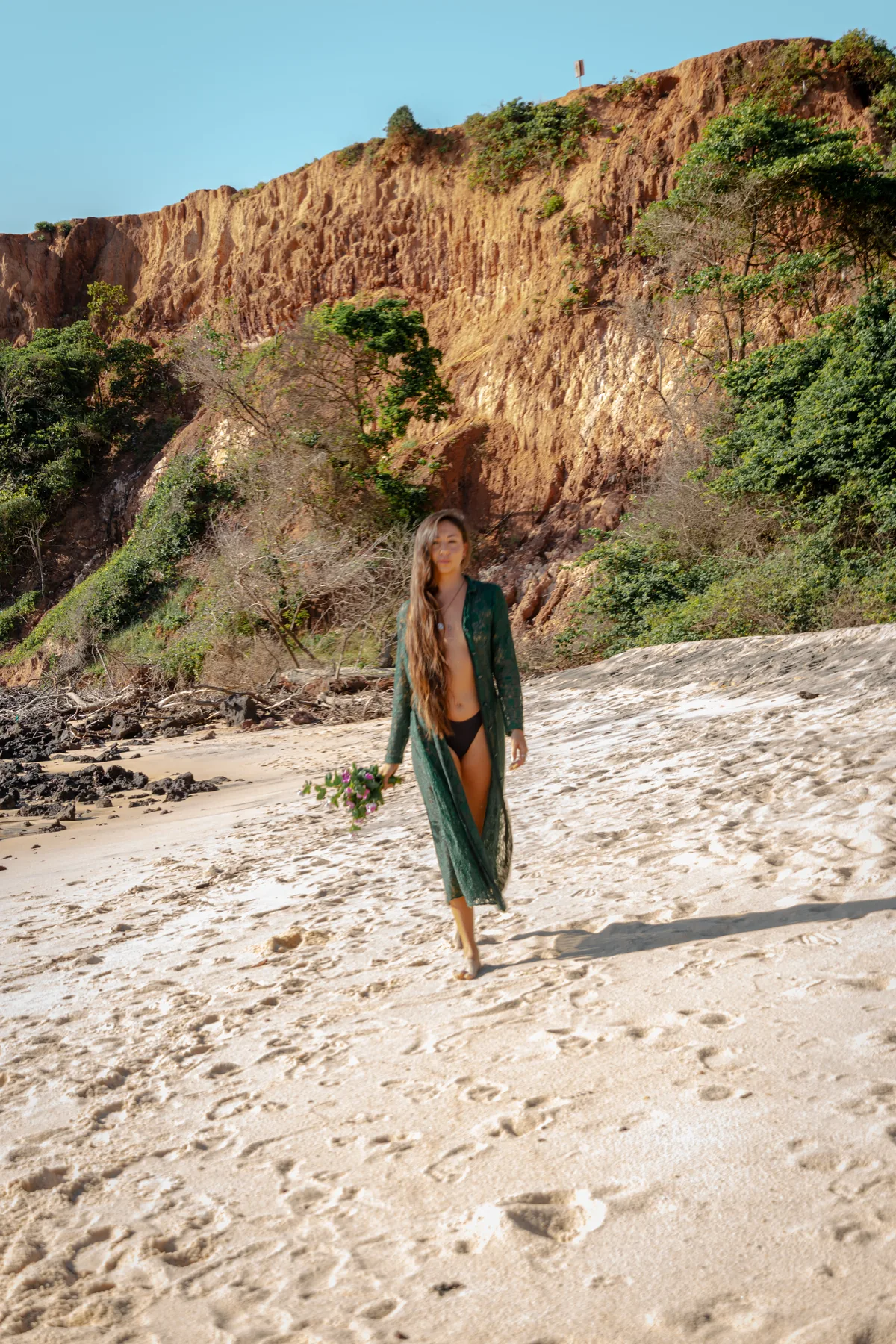 Mujer caminando en una playa clara frente a acantilados rojizos