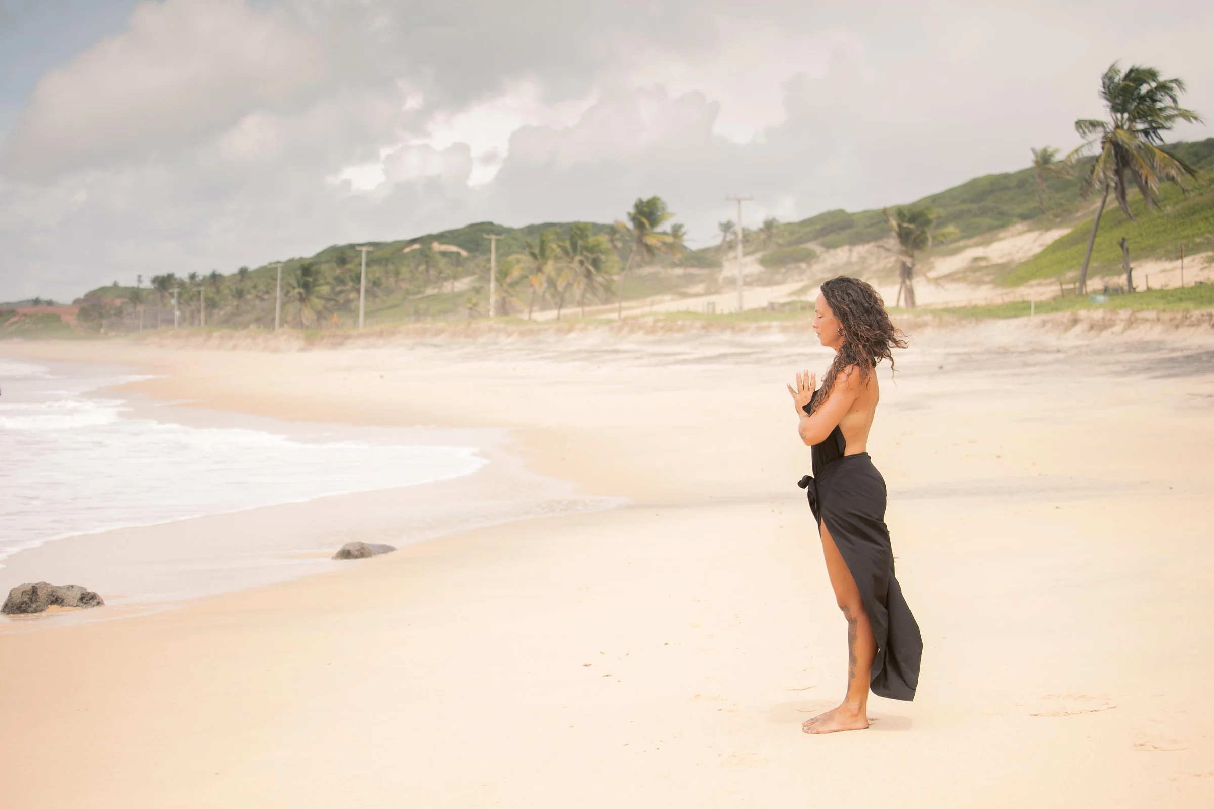 Mujer de vestido negro en la playa con gesto de pausa frente al mar