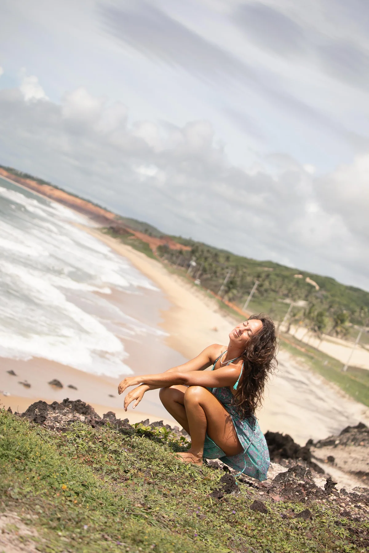 Mujer sentada sobre rocas frente a una playa y acantilados