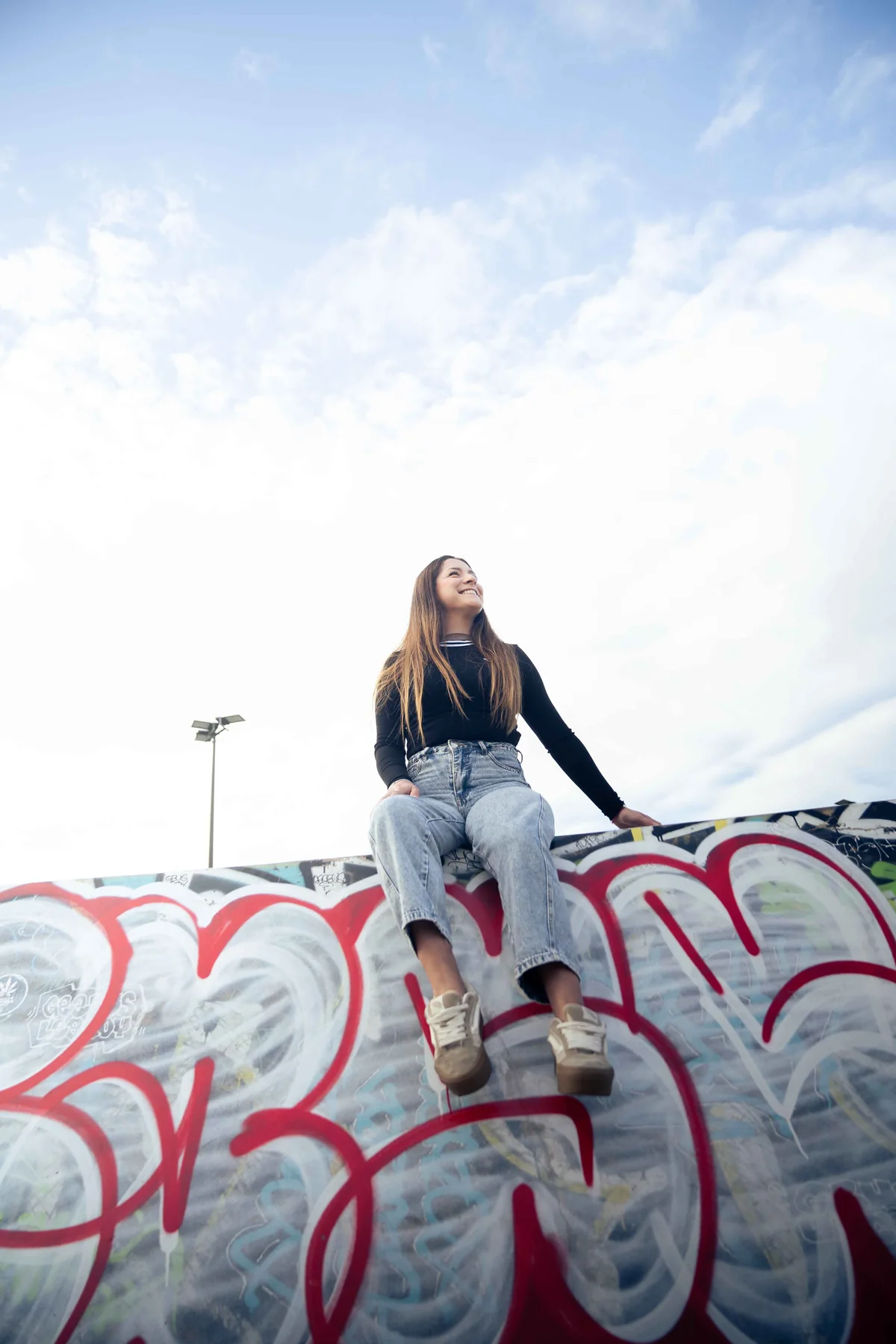 Retrato urbano sentada sobre un muro con grafiti y cielo amplio