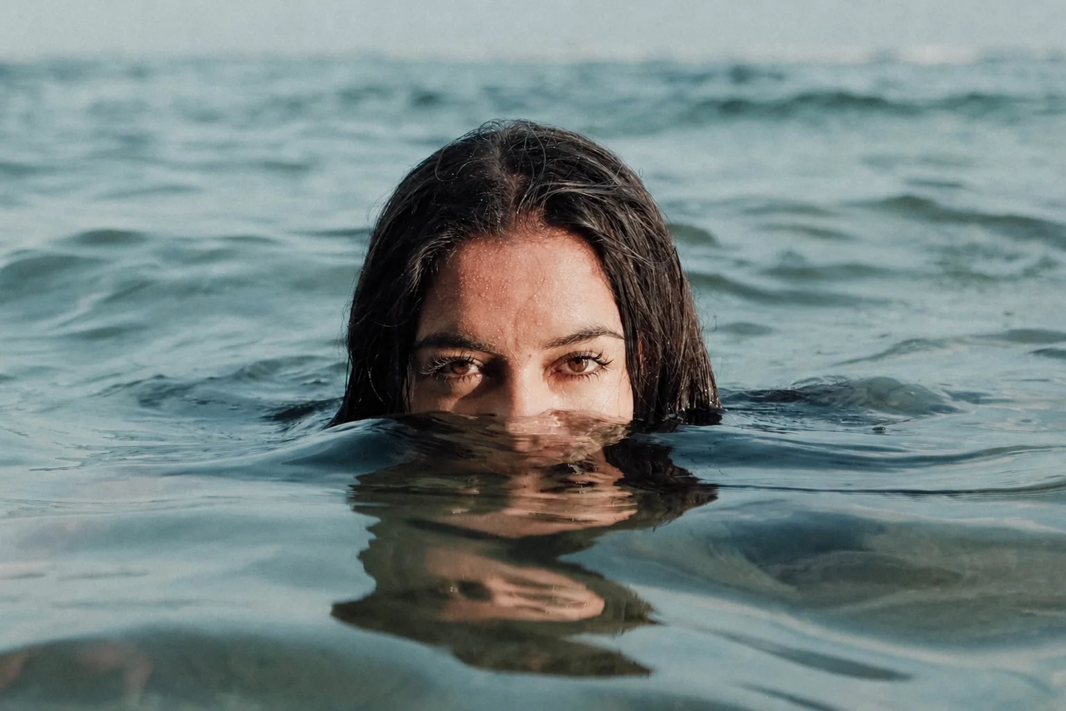 Mimi mirando a cámara desde el agua con el rostro parcialmente sumergido