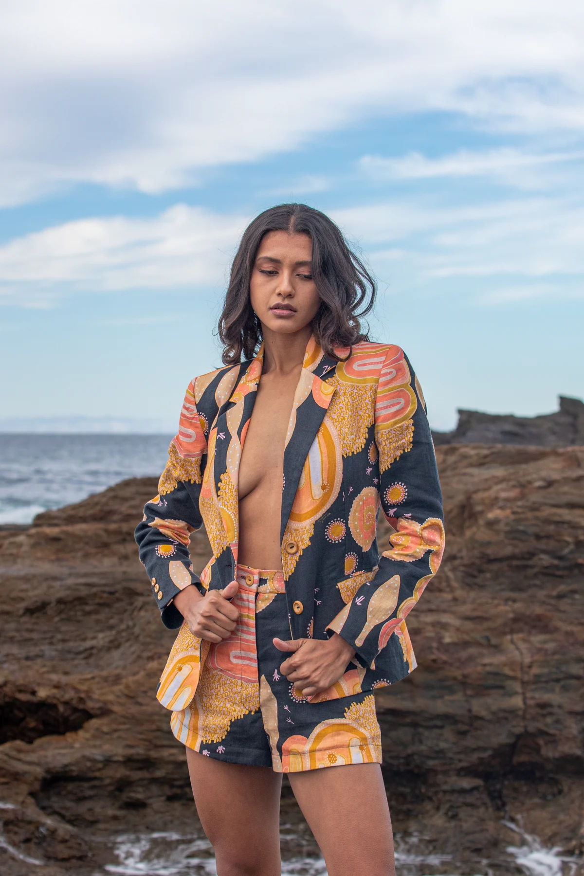 Retrato editorial con traje estampado frente a rocas costeras