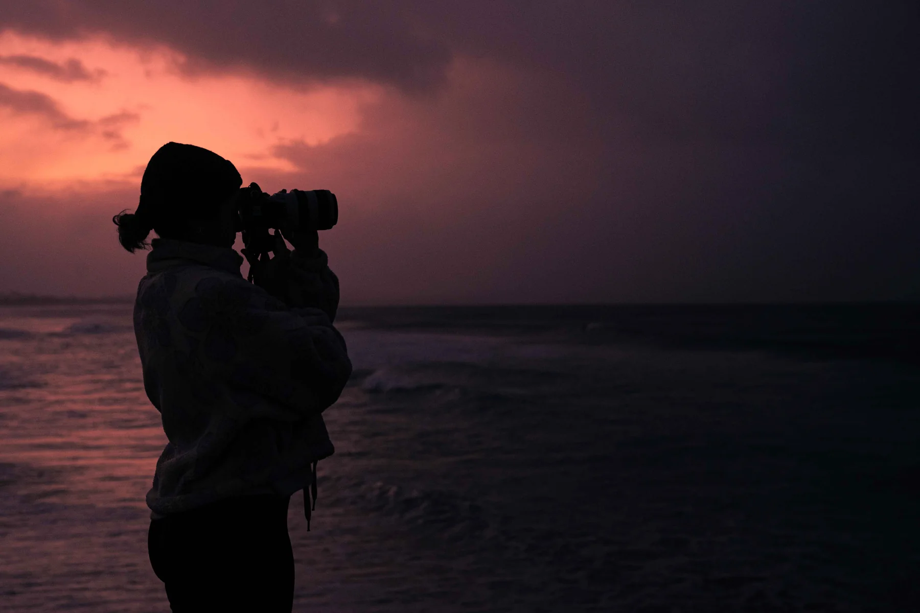 Silueta de fotógrafa mirando por la cámara al atardecer en la playa