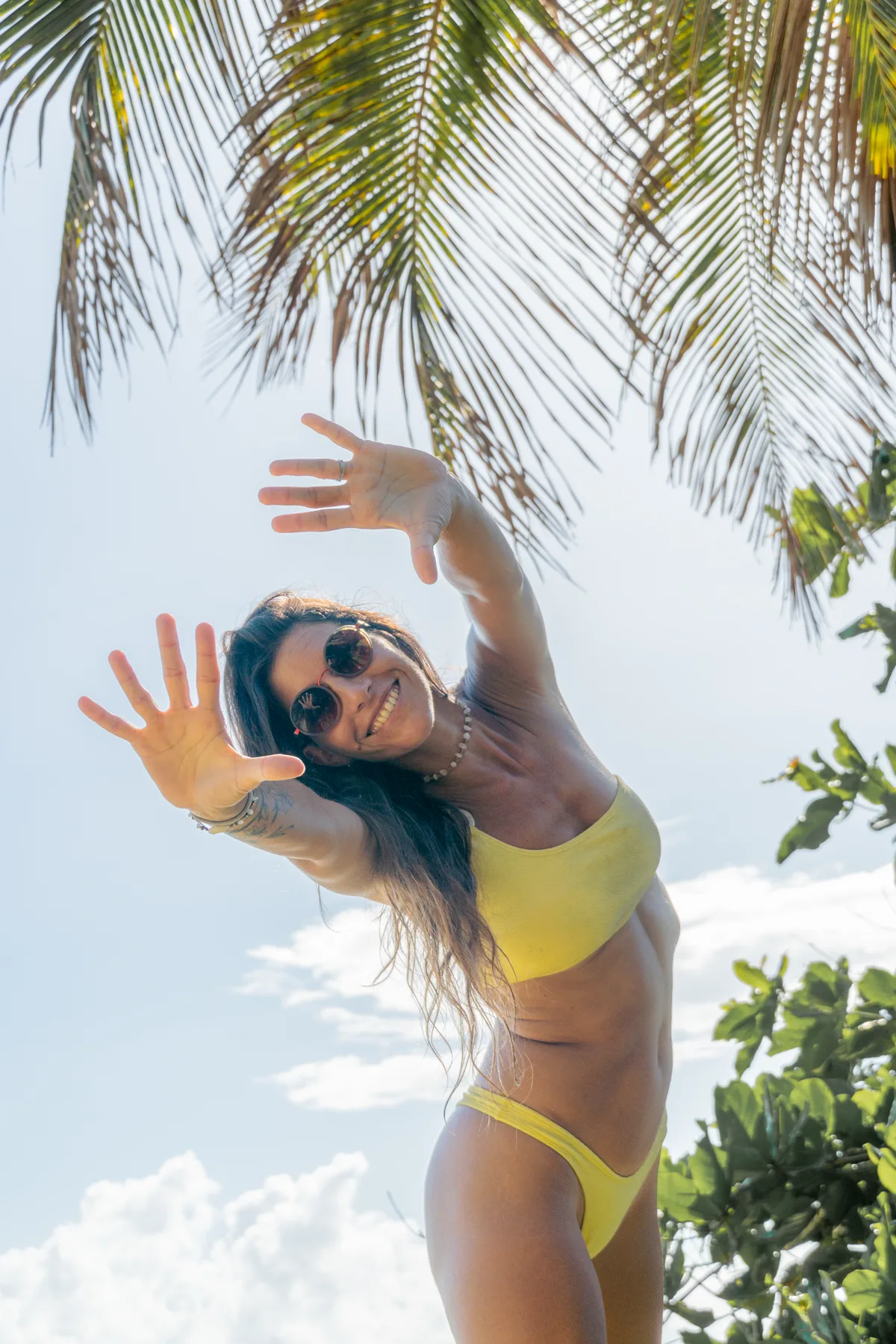 Retrato sonriente bajo palmeras con bikini amarillo
