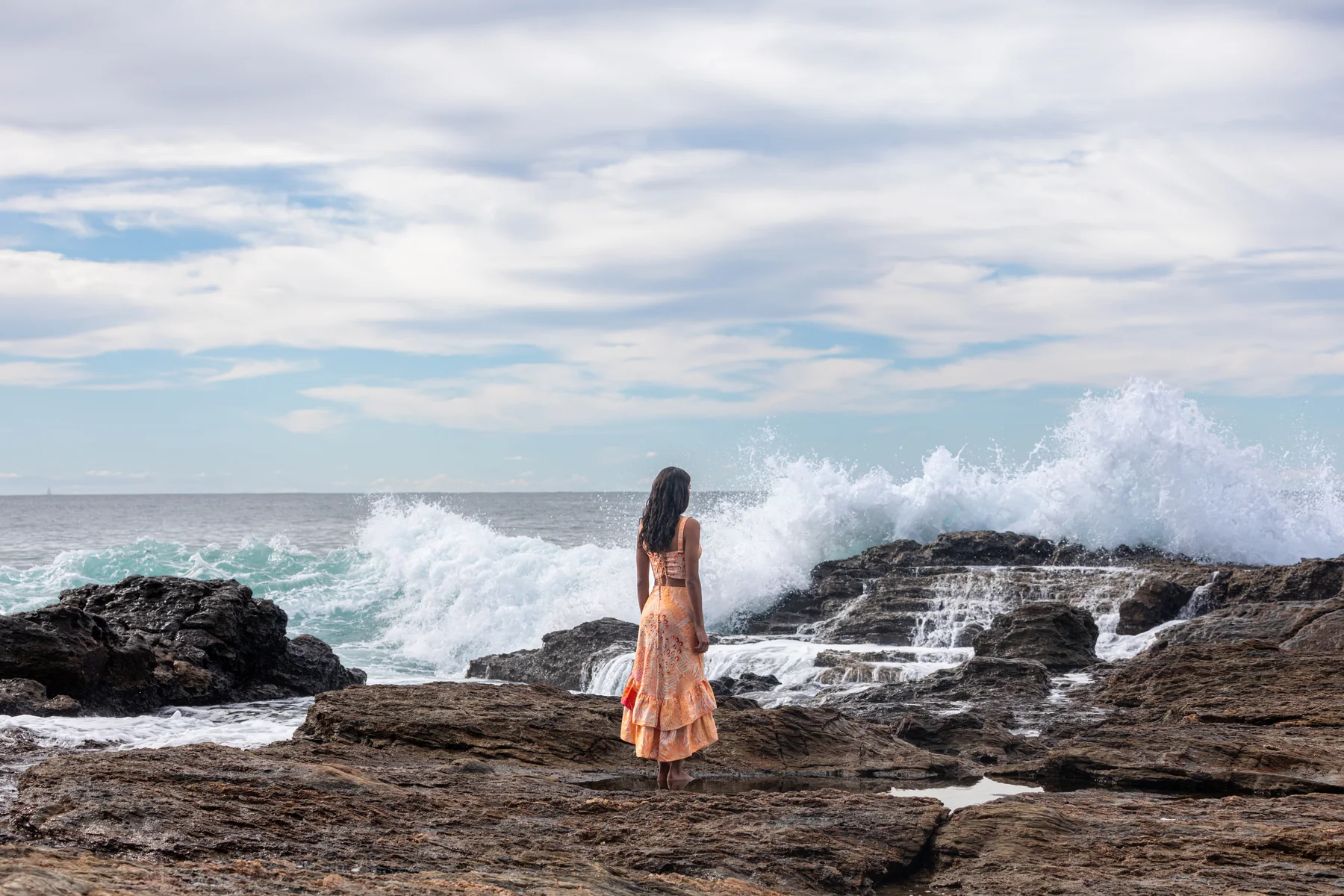 Mujer frente a una ola rompiendo sobre rocas